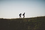 Two hikers holding hands up on a hill