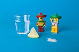 A shot of tequila, a lime, a small pile of salt, and two Mexican looking lego figures