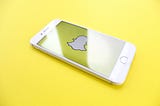 iPhone on yellow surface displaying Snapchat logo