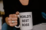 A sitting woman holds a “World’s Best Boss” mug