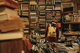 A person looking at disorganized book shelves, back toward the camera.