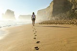 A woman walking along a beach, leaving footprints in the sand