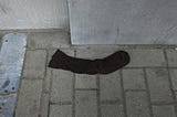 Single sock on a brick floor, next to a solid wall.