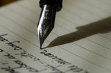 Image of a black fountain pen being used to write in cursive on a white sheet of lined paper