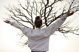 Person exercising with arms raised in front of a tree