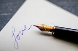The word “love” written in blue on white paper next to a gorgeous calligraphy pen.