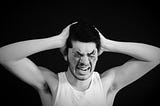 A man in a white cotton vest has his hands on his head, eyes covered and appears to be screaming