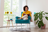 Woman curled up in a chair, thinking, with a pen and notebook.