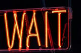 A neon sign saying ‘wait’