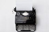 Black vintage Adler ‘Favorit’ typewriter with a blank page against a blank white background.