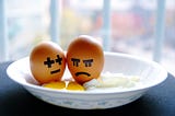 Couple of eggs in a plate with painted faces. One of the eggs has a painted-on frustrated face.