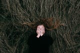 Woman lies in a field, covering her faces with her hands.