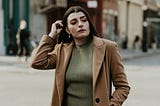 woman in brown coat standing on sidewalk during daytime
