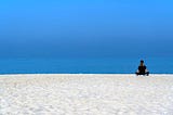 Someone meditating on a beach.