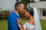 Man in blue suit kissing woman in bridal gown on forehead