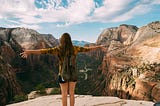 A mountain climber uses her energy to reach the peak and opens her arms wide with joy