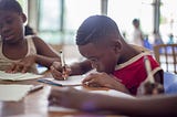 A boy writing in a book. His focus is as if he were writing some lines of codes.