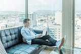 A young man sitting in his apartment with urbanistic view through the window