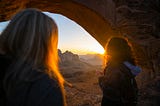 Two women looking out at the sunset under an old arch, the world full of possibilities