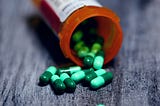 Pill bottle on its side with green capsules spilling out