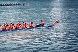 Two teams of dragon boats in orange shirts, rowing through a river