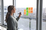 Woman holding a pen in front of some post it notes on a window.