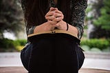 A woman sat outside with praying hands leaning on a bible.