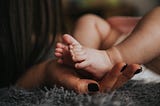 A mother’s hand holding the foots of her only child.