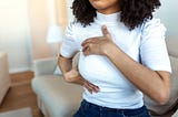 Black woman hand-checking lumps on her breast for signs of breast cancer