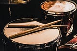 A well-worn drum set with a pair of drumsticks resting on it.