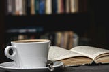 Coffee cup sitting next to an open book on a table