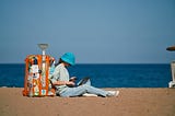 Girl remote worker sits on the beach with a suitcase and works while on vacation. IT specialist working online in time of eurotrip