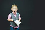 A little boy holding a book and looking surprised