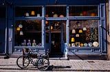 A blue storefront with lamps visible in the windows and a bike parked in front of the store.