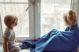 Two blond children looking out the window
