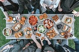 A family gathers around a wooden picnic table filled with delicious food.