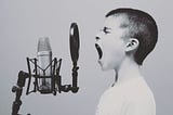 Black & white photo of 8 (or so) year old boy screaming into a microphone