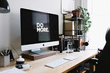 Modern office setup with a large monitor that reads “DO MORE” in white on a black background.