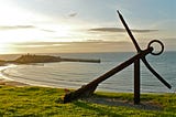 calm sea. anchor resting akilter on shore, sunrise