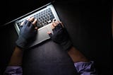 Hands in fingerless gloves on a keyboard. Gives the impression of illegal goings on.