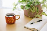 [image description: A wood desk with a leafy trailing plant, a notebook open to a blank page, and a mug that says “go get ‘em.”] post contains an affiliate link