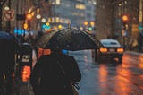 Man with an umbrella, rainy street in a city. Dusk.
