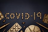 Golden syringes and pills arranged to spell covid-19