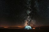 A blue tent, lit from within, has the Milky Way above it