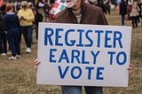 Man holding a sign that says “Register early to vote”
