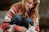 Photo of an attractive young woman leaning down to pet a white and brown cat.
