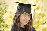 Head shot of female in cap and gown, smiling shyly.