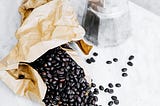 Fair Trade coffee beans spilling out of a paper bag onto counter next to a French press