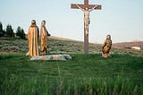 Statues depicting Jesus on a cross and three witnesses, one of them kneeling.