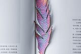 A lavendar and pastel-colored feather marks the pages of a book.